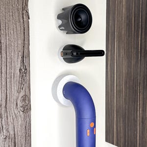 May include: A white wall with three objects mounted on it. The top object is a black speaker with a white logo that says "Q-Sound". The middle object is a black and silver device with a white base. The bottom object is a blue and white handrail with two orange buttons.