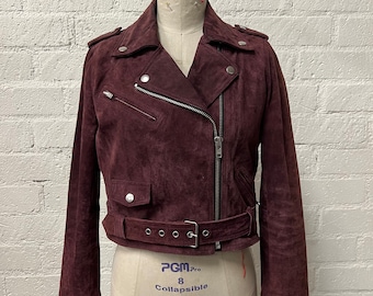 May include: A burgundy suede moto jacket with a zipper closure, a belt, and two pockets. The jacket has a classic biker style.