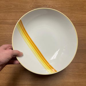 May include: A white ceramic bowl with a yellow and orange stripe design.