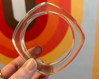 May include: A clear plastic bangle bracelet with a square shape.