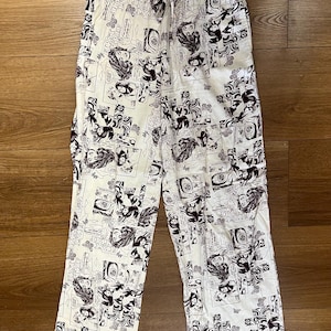 Puede incluir: Pantalón blanco con estampado de cómic en blanco y negro. El estampado presenta imágenes de personas y texto.