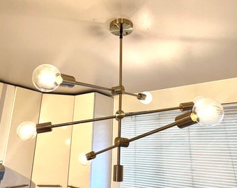 May include: A modern, multi-arm chandelier with six globe-shaped light bulbs. The fixture has a brushed brass finish and is suspended from the ceiling. The bulbs are clear, providing bright illumination.