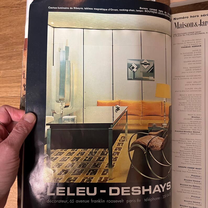 May include: A living room interior design featuring a large, modern, silver-toned floor lamp, a black and glass coffee table, a yellow sofa, a black and chrome rocking chair, and a geometric abstract painting on the wall. The room has a patterned carpet and wood paneling.