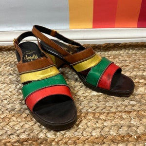 May include: A pair of brown, yellow, green, and red leather platform sandals with a slingback strap. The sandals are labeled "Amalfi" on the side.