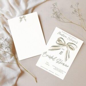 May include: A white bridal shower invitation with a green and white striped bow. The invitation reads "Please join us to celebrate Madison Johnson's Bridal Shower" with the date "June 18" and the time "1:30PM". The invitation also includes the location "Notting Hill Country Club, 27 Orchard Rd, North Gallen, NC 28701" and the RSVP information "By June 10th".