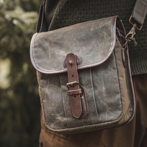 Peut inclure: Sac en bandoulière en toile cirée vert olive avec garnitures en cuir marron. Le sac est doté d'un rabat avec une boucle en cuir et d'un fermoir en métal pour la bandoulière. Conçu pour transporter des objets.