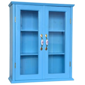 Op de afbeelding: Een lichtblauwe wandkast met twee glazen deuren. De kast heeft twee planken en decoratieve bloemenhandgrepen. De scharnieren en het beslag zijn goudkleurig. De kast is geschilderd in een effen, lichtblauwe kleur.