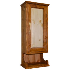 Könnte beinhalten: Ein hoher Wandschrank aus Holz mit einer Tür und einem Regal darunter. Der Schrank ist aus hellem und dunklem braunem Holz gefertigt, mit einer helleren Holzplatte in der Tür. Der Schrank hat ein klassisches Design.