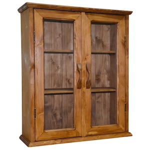 Op de afbeelding: Een houten wandkast met twee glazen deuren. De kast is gemaakt van lichtbruin hout en heeft twee planken aan de binnenkant. De deuren hebben houten handgrepen en zijn omlijst door hetzelfde hout.
