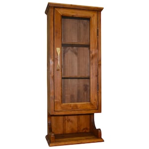 Op de afbeelding: Een hoge, houten wandkast met een glazen deur en een klein plankje eronder. De kast is gemaakt van gebeitst hout en heeft een eenvoudig, rustiek ontwerp. De kast is ongeveer 30 cm breed en 91 cm hoog.