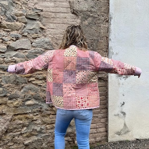 Puede incluir: Una chaqueta acolchada de patchwork rosa y roja con estampado floral. La chaqueta tiene cuello y mangas largas.