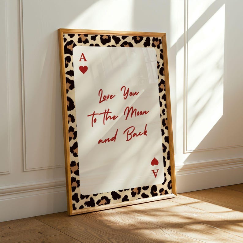 May include: A framed print featuring a playing card design with a leopard print border. The card is an Ace of Hearts, with the text "Love You to the Moon and Back" in red script. The frame is a light brown color.