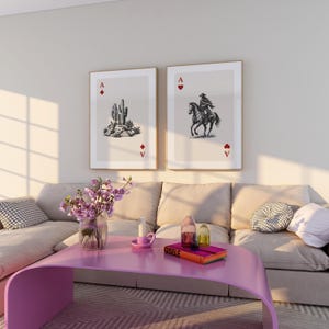 K&ouml;nnte beinhalten: Zwei gerahmte Kunstdrucke, die Spielkarten-Asse darstellen. Einer zeigt einen Kaktus, der andere einen Cowboy auf einem Pferd. Sie h&auml;ngen &uuml;ber einem rosa Couchtisch mit einer Blumenvase und dekorativen Gegenst&auml;nden.