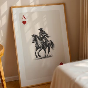 K&ouml;nnte beinhalten: Gerahmter Kunstdruck mit dem Pik-Ass. Das Kartendesign zeigt eine Schwarz-Wei&szlig;-Illustration eines Cowboys auf einem Pferd. Das Kunstwerk ist vor einem neutralen Hintergrund platziert, mit den roten Herzsymbolen und dem Buchstaben "A".