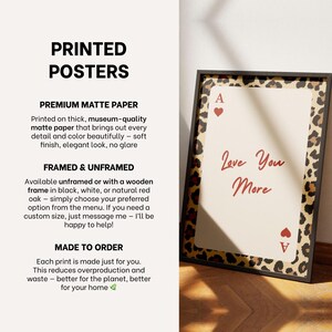 May include: A framed print featuring a playing card design with the text "Love You More" in red script. The frame is black with a leopard print border. The text "PRINTED POSTERS" is at the top.
