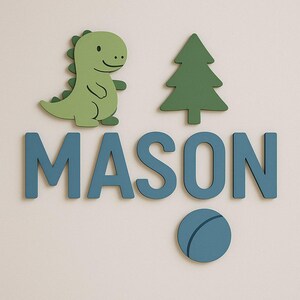 May include: A wall decoration with the name "MASON" in blue letters, alongside a green dinosaur, a green tree, and a blue circle. The dinosaur and tree are cut-out shapes, creating a playful, decorative theme for a child's room.