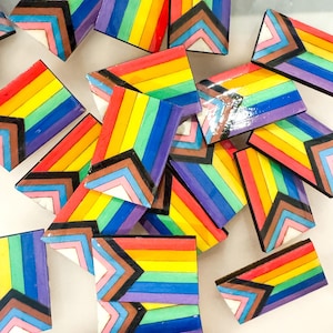 May include: A collection of colorful wooden rainbow-themed tiles with a black outline. Each tile features a geometric pattern of stripes and triangles.