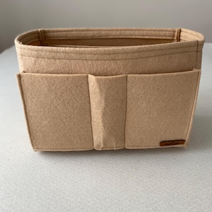 Op de afbeelding: Beige felt organizer met meerdere vakken en een klein label met de tekst "Keep It Clean".