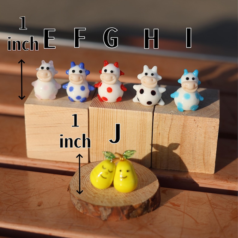 May include: Six miniature glass cow figurines with different colored polka dots, each measuring 1 inch tall. The cows are arranged on wooden blocks labeled E through I. A pair of yellow glass pears are on a wooden slice labeled J.