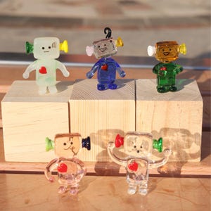 May include: Five glass robot figurines with different coloured bodies and antennas. Each robot has a red heart on its chest.