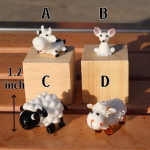 May include: Four glass animal figurines on wooden blocks. A black and white cow, a white rabbit, a black and white sheep, and a white sheep with brown legs. The blocks are labeled A, B, C, and D. The blocks are 1.2 inches tall.