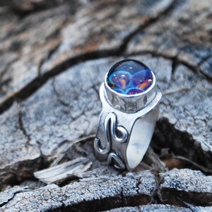 May include: A silver ring with a swirling design and a round, iridescent blue and purple gemstone.