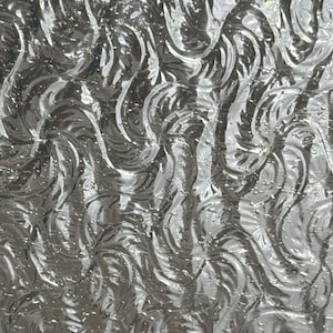 May include: A sheet of clear, textured glass featuring a repeating pattern of raised, swirling, flame-like shapes. The surface has a glossy, reflective quality that creates light and shadow across the intricate, embossed, organic curves.