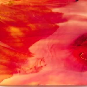 May include: A sheet of smooth, semi-translucent glass featuring a vibrant, swirling blend of bright red, deep magenta, and warm orange hues. The surface displays a marbled, fluid pattern with varying color density and light diffusion throughout.