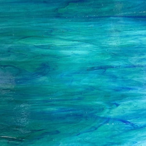 May include: A sheet of stained glass featuring a swirling pattern of vibrant turquoise, deep ocean blue, and light aquamarine hues. The surface displays a smooth, semi-translucent texture with organic, flowing color gradients throughout the material.