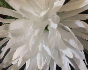 May include: Close-up of a white artificial flower with long, thin petals radiating from a central point. The flower has a layered texture and a delicate appearance, with hints of green at the center.