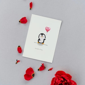 Carte de saint valentin disant je t'aime avec un pingouin mignon tenant un ballon en cœur pour elle ou pour lui à télécharger et imprimer.
