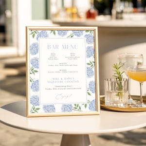 May include: A framed bar menu with a gold border, featuring a floral design of blue hydrangeas. The menu lists beer, wine, spirits, and mixers, with a signature cocktail recipe. The words "BAR MENU" are at the top.