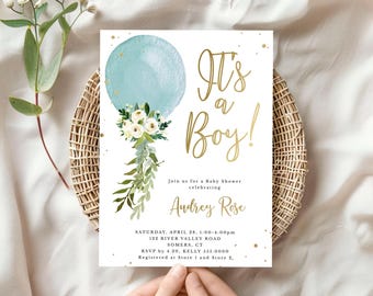 May include: A white rectangular baby shower invitation card featuring a watercolor light blue balloon with a bouquet of white flowers and green leaves. The text reads It's a Boy! in gold script, followed by event details for Audrey Rose.