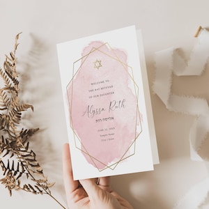 May include: A white Bat Mitzvah invitation card featuring a pink watercolor wash background enclosed in a gold geometric frame. The text reads Welcome to the Bat Mitzvah of our daughter Alyssa Ruth, with Hebrew text, a Star of David, and date details.