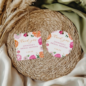 Puede incluir: Dos etiquetas florales de agradecimiento para una despedida de soltera. Una es cuadrada, la otra redonda. Ambas tienen un borde floral de flores rosas y naranjas. El texto dice "Thank you, Jennifer's Bridal Shower, 4.28.XX". Cuelgan de una cuerda.