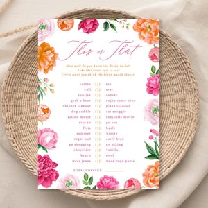 May include: A floral-themed bridal shower game card with the text "This or That." The card features pink and orange flowers and a list of choices like "coffee or tea." The card is on a woven tray.