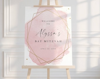 May include: A rectangular welcome sign on a wooden easel featuring a soft pink watercolor wash background, a thin gold geometric frame, and black text that reads: Welcome to Alyssa's Bat Mitzvah, April 28, 20XX, with small gold speckles.