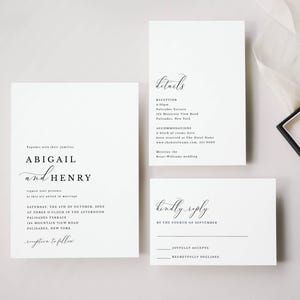 May include: A minimalist wedding stationery set. Three white cards with black text, including the names "Abigail and Henry". A ring box and wedding rings are also visible, creating a clean aesthetic.