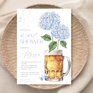 Op de afbeelding: Een uitnodiging voor een bruidsdouche met een aquarel illustratie. Het ontwerp bevat blauwe hortensia's, een bierpul en de tekst "Join us at a bridal shower honoring Alyssa". De uitnodiging ligt op een gevlochten dienblad.