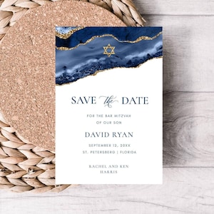 Puede incluir: Una tarjeta Save the Date azul marino y dorada para un Bar Mitzvah. El diseño presenta un fondo de acuarela azul con detalles dorados y una Estrella de David. El texto incluye los detalles del evento: David Ryan, 12 de septiembre de 20XX, St. Petersburg, Florida.