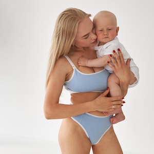 Op de afbeelding: Een lichtblauwe tweedelige lingerieset bestaande uit een bralette met ronde hals en een slip met hoge taille. Beide stukken zijn voorzien van een contrasterende witte bies langs de randen. De bralette heeft verstelbare schouderbandjes.