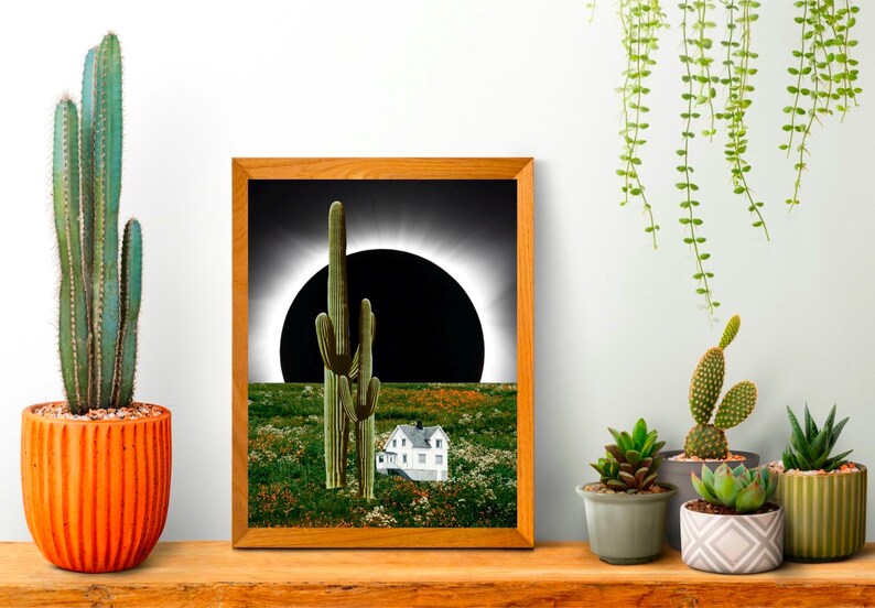 Pu&ograve; includere: Una stampa incorniciata di un paesaggio desertico con due alti cactus e una piccola casa bianca in primo piano. Il sole &egrave; parzialmente eclissato dalla luna, creando un cerchio scuro nel cielo.