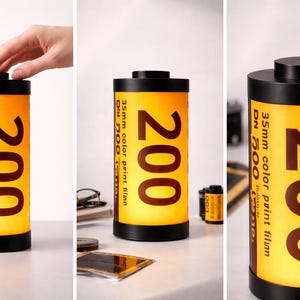 May include: A cylindrical lamp resembling a 35mm film canister. The lamp has a black top and base, with a yellow and orange body. The number "200" is prominently displayed, along with text indicating "35mm color print film".