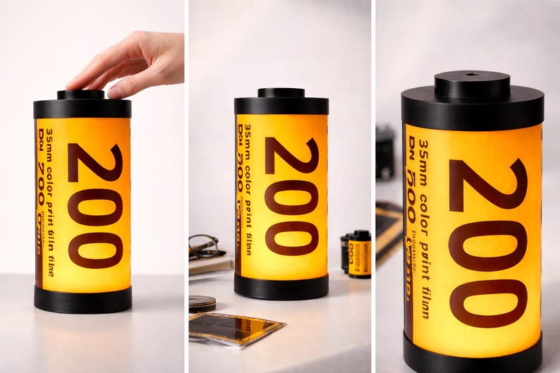 May include: A cylindrical lamp resembling a 35mm film canister. The lamp has a black top and base, with a yellow and orange body. The number "200" is prominently displayed, along with text indicating "35mm color print film".