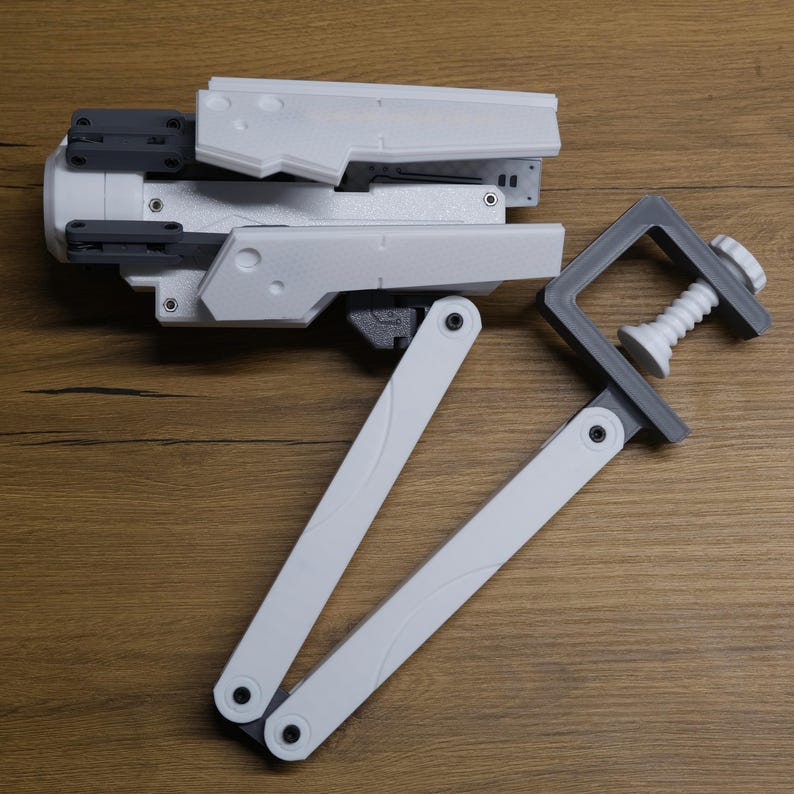 K&ouml;nnte beinhalten: Ein wei&szlig;er, artikulierter Roboterarm mit einer grauen Klemme. Der Arm besteht aus mehreren Abschnitten, die bewegt und angepasst werden k&ouml;nnen. Die Klemme hat eine Schraube, die zum Befestigen eines Objekts angezogen werden kann.