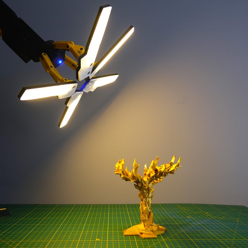 K&ouml;nnte beinhalten: Eine goldfarbene, abstrakte Baumskulptur mit einem facettenreichen Design wird von einer mehrarmigen LED-Leuchte beleuchtet.