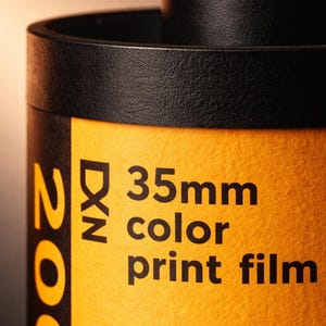 May include: Close-up of a 35mm color print film canister. The film canister is black with a yellow label. The label has the text "35mm color print film" in black. The film is 200 speed.
