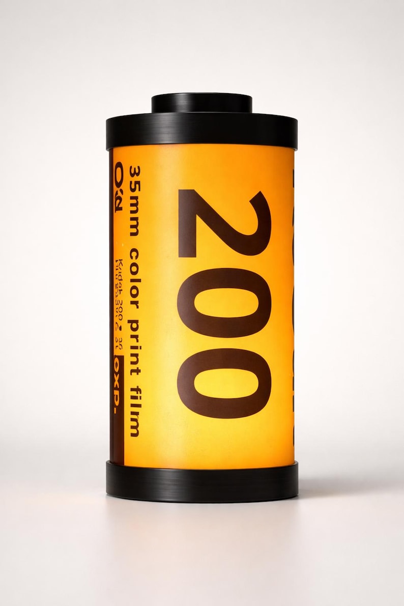 May include: A cylindrical roll of 35mm color print film, labeled "200". The film canister is primarily yellow with black text and accents. The top and bottom are black. The film is labeled "Kodak 200" and "EXP."