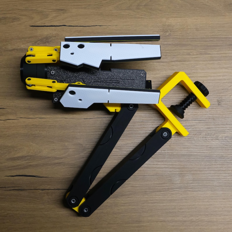 K&ouml;nnte beinhalten: Ein schwarz-gelber 3D-gedruckter Roboterarm mit einer Klemme. Der Arm besteht aus mehreren Segmenten, die in verschiedene Positionen eingestellt werden k&ouml;nnen. Der Arm ist f&uuml;r eine Vielzahl von Aufgaben konzipiert, wie z. B. das Halten von Objekten, das Bewegen von Objekten und das Ausf&uuml;hren anderer Aufgaben.