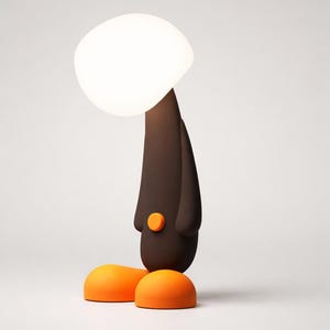 Può includere: Una lampada da tavolo stravagante con un corpo marrone, piedi arancioni e una grande luce bianca di forma ovale. La lampada presenta un piccolo pulsante arancione ed è progettata con un'estetica da cartone animato. La lampada è alta circa 30 cm.